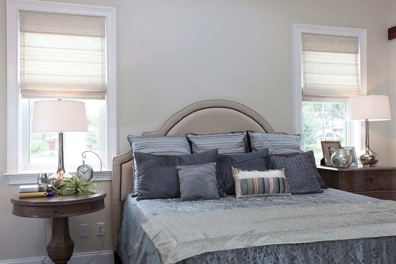 Grey roman shades next to a bed.